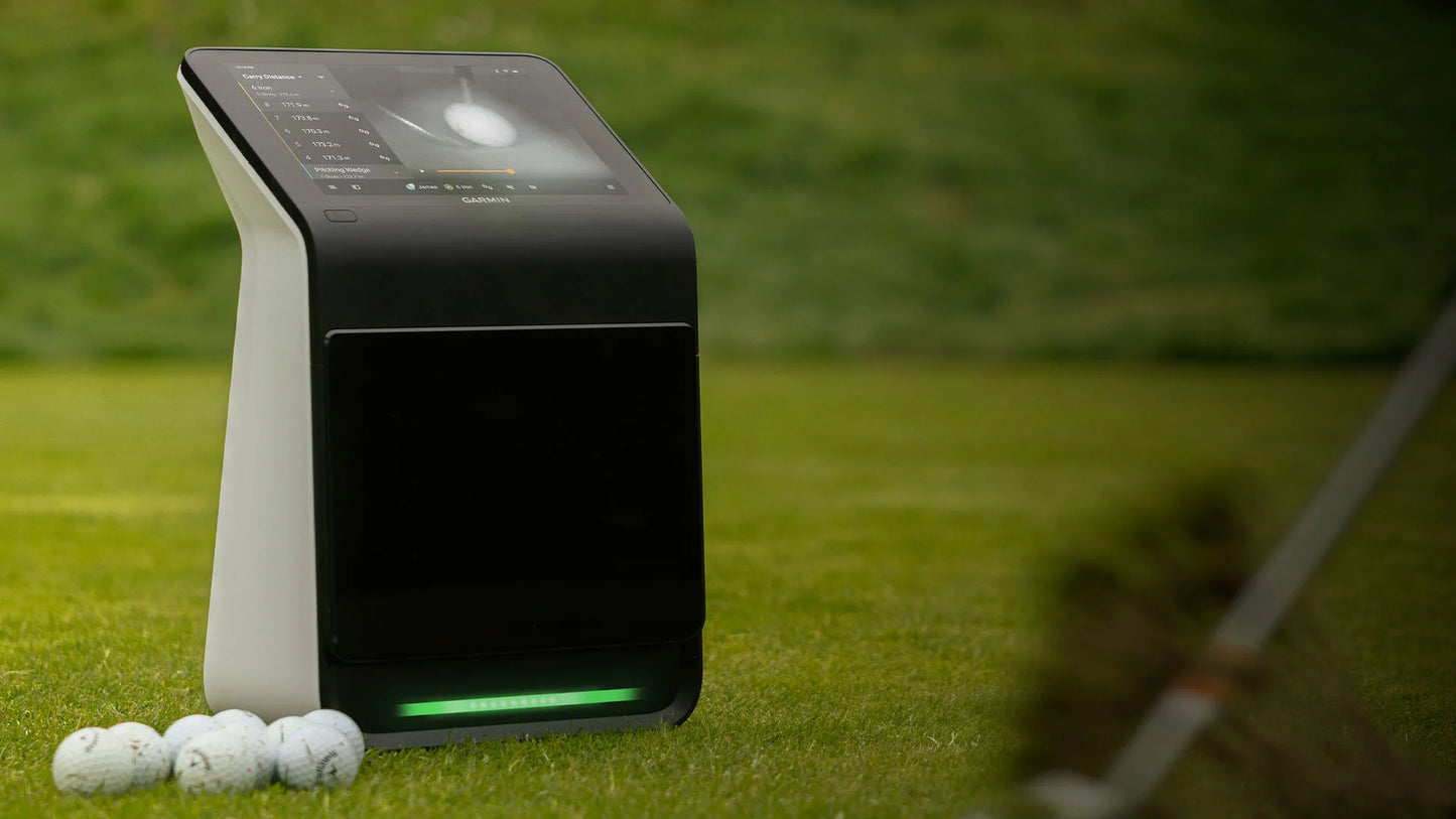 Garmin Approach R50 golf simulator on grass with golf balls, featuring a touchscreen display for metrics and courses.