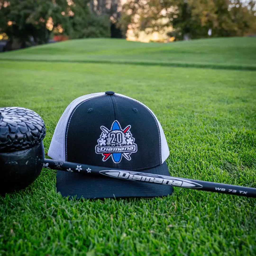 Mitsubishi Diamana cap resting on green grass next to a Diamana WB wood shaft, showcasing golf gear.