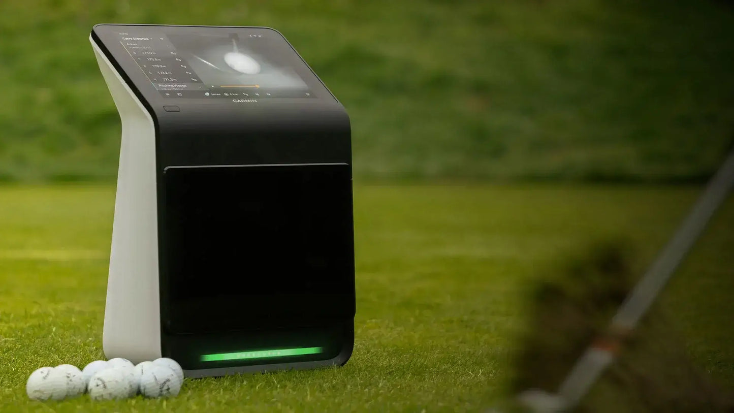 Garmin Approach R50 golf simulator on grass with golf balls, featuring a touchscreen display for metrics and courses.