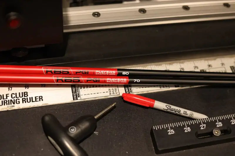 KBS PGI graphite shafts in black and red resting on a golf club ruler, showcasing performance specifications.