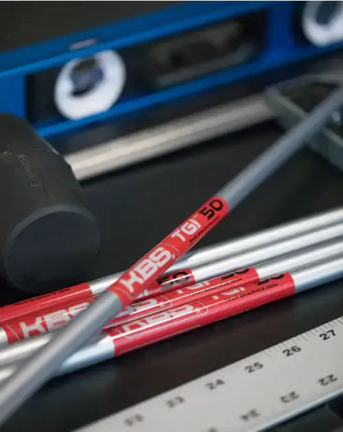 KBS TGI Tour Graphite Iron Shafts displayed on a workshop table with tools and measuring instruments.
