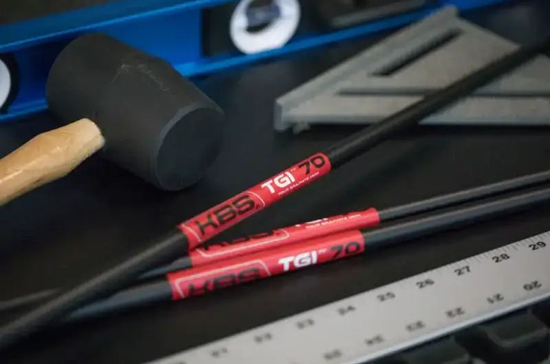 KBS TGI Tour Graphite Iron shafts on workbench with mallet and measuring tools, showcasing innovative golf technology.