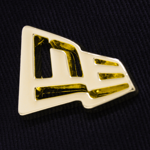 Close-up of a gold metal badge featuring the New Era logo on a dark fabric background.