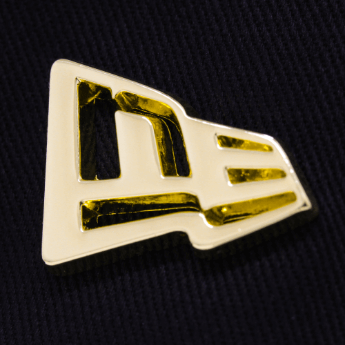 Close-up of a gold metal badge featuring the New Era logo on a dark fabric background.