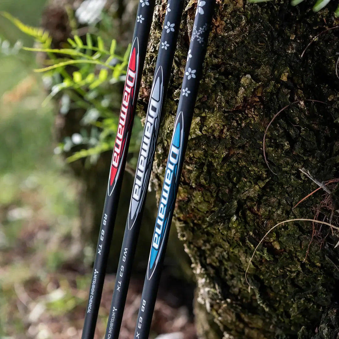 Close-up of Mitsubishi Diamana wood shafts with red and blue accents against a tree backdrop.