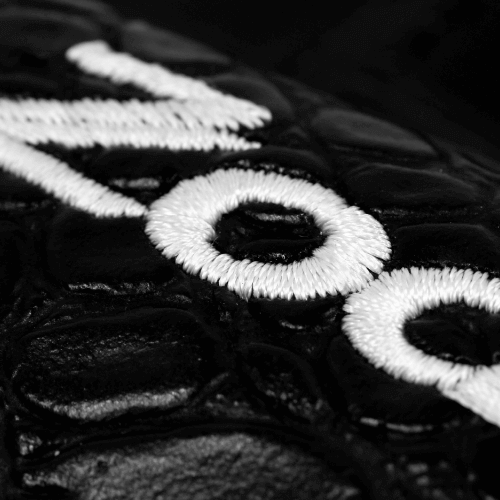 Close-up of Zodia Iron Cover's embroidered logo on a textured black fabric background.
