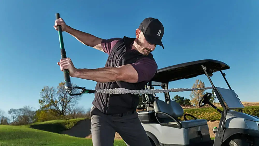 Man training golf swing with GolfForever™ Swing Trainer+ near a golf cart outdoors.