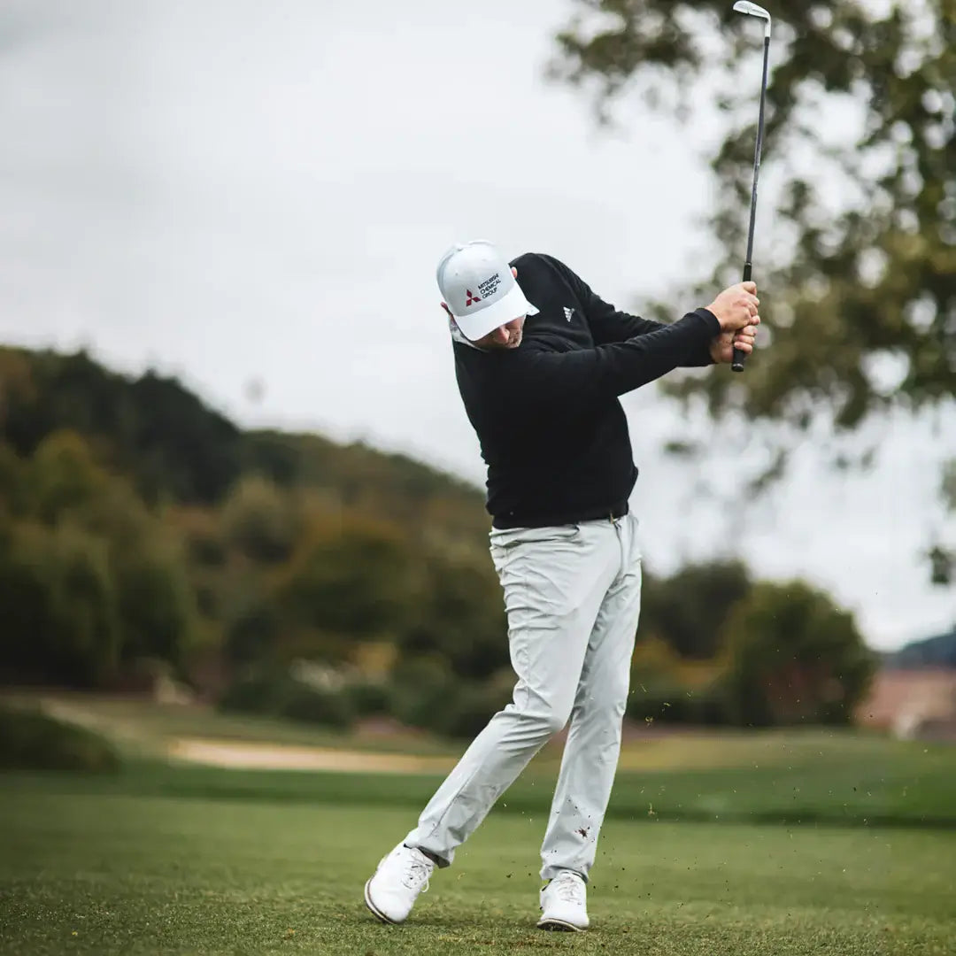 Golfer in a black sweater and grey pants executing a swing on the course with a Mitsubishi MMT Taper Iron Shaft club.