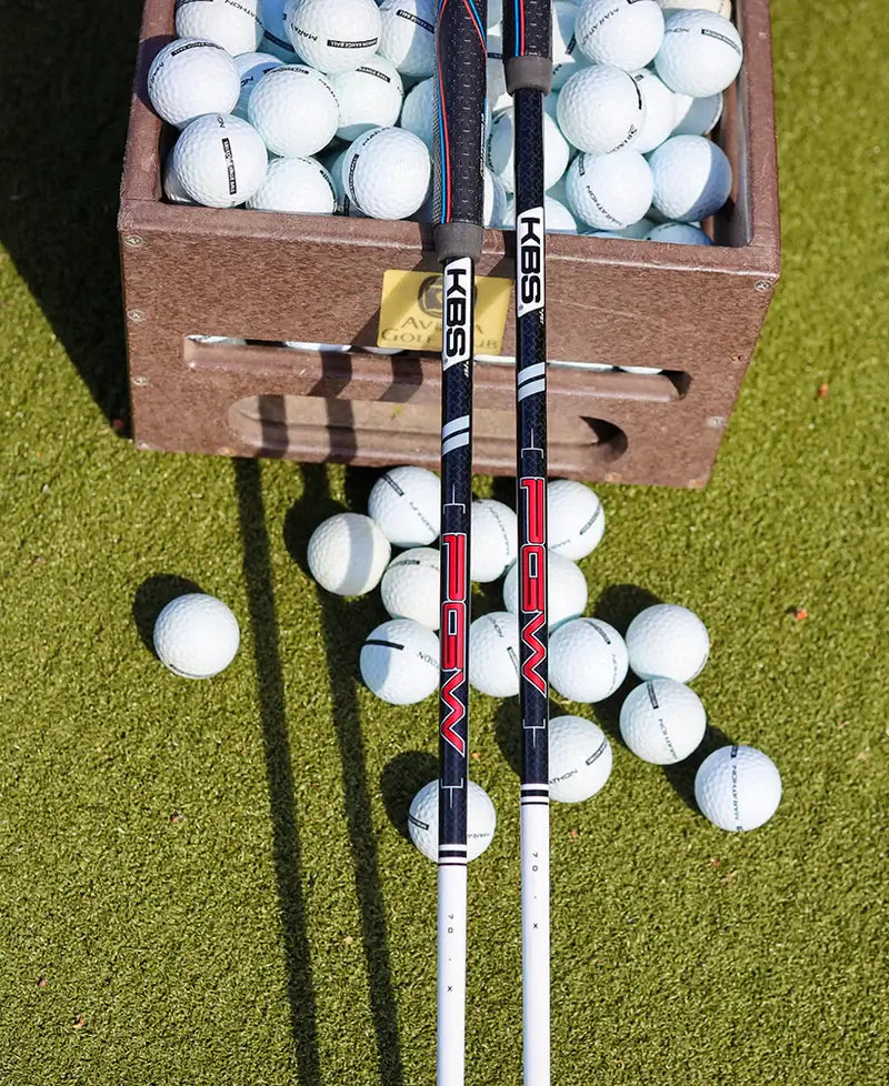 KBS PGW graphite wood shafts displayed beside a box of golf balls on a green surface.