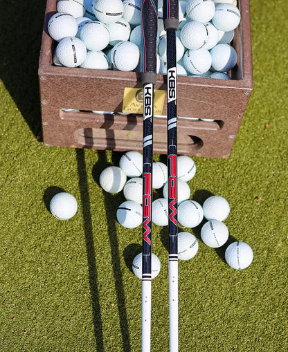 KBS PGW graphite wood shafts displayed beside a box of golf balls on a green surface.