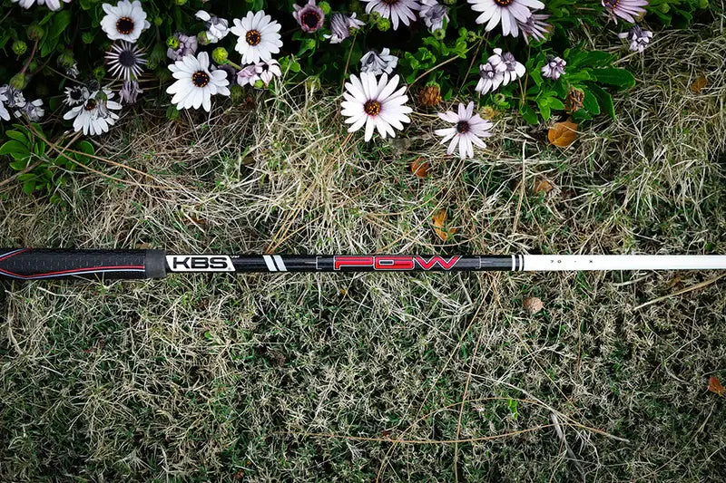 KBS PGW graphite wood shaft laying on grass with flowers, ideal for enhancing golf swing performance.