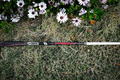 KBS PGW graphite wood shaft laying on grass with flowers, ideal for enhancing golf swing performance.
