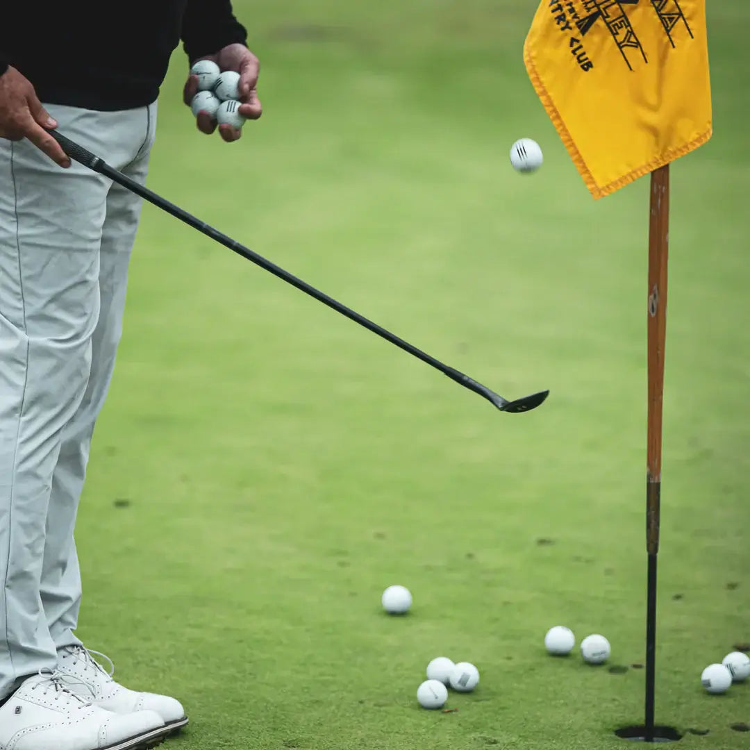 A golfer practicing with the Mitsubishi MMT Scoring Wedge near the flag on the green, holding several golf balls.
