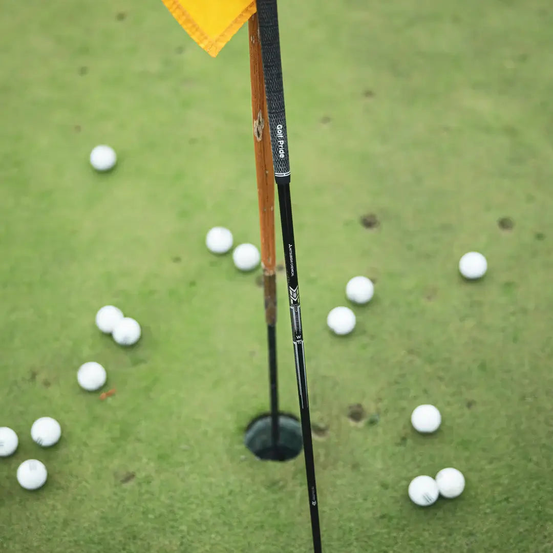 Mitsubishi MMT Scoring Wedge near golf hole with golf balls, showcasing Metal Mesh Technology for better feel and responsiveness.