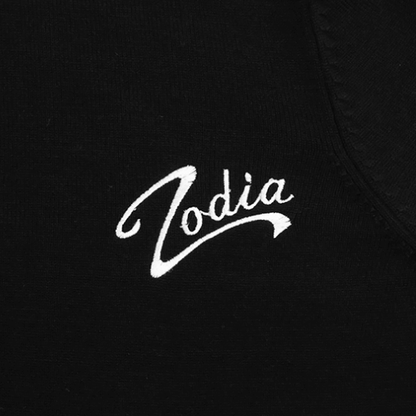 Close-up of 'Zodia' logo in white embroidery on a black crewneck sweater fabric.