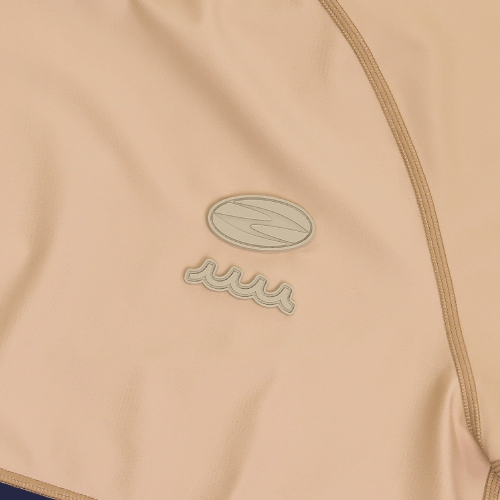 Close-up of the Zodia muta mock neck shirt showing the stylish logo on soft beige fabric.