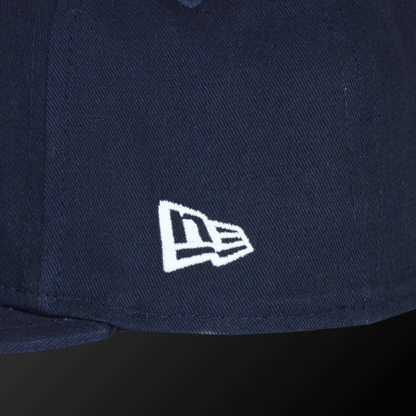 Close-up of the white New Era logo on a Zodia navy flat visor cap.