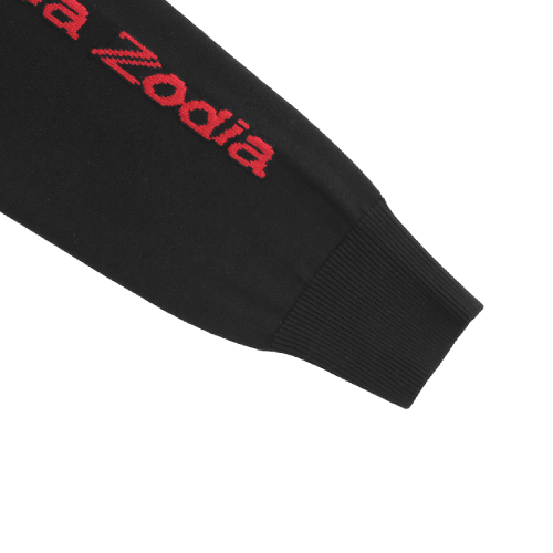 Close-up of Zodia Zip-Up sweater sleeve featuring red logo against black knit fabric.