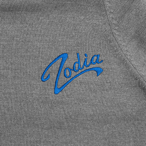 Close-up of Zodia logo in blue embroidery on a gray knit fabric, showcasing stylish branding.